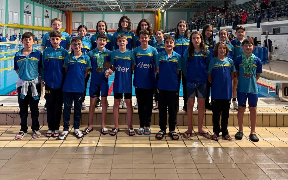 The Club Natación Axarquía alevín team wearing medals, posing at the indoor pool of the Andalusian winter alevín championship in Cádiz, 2026