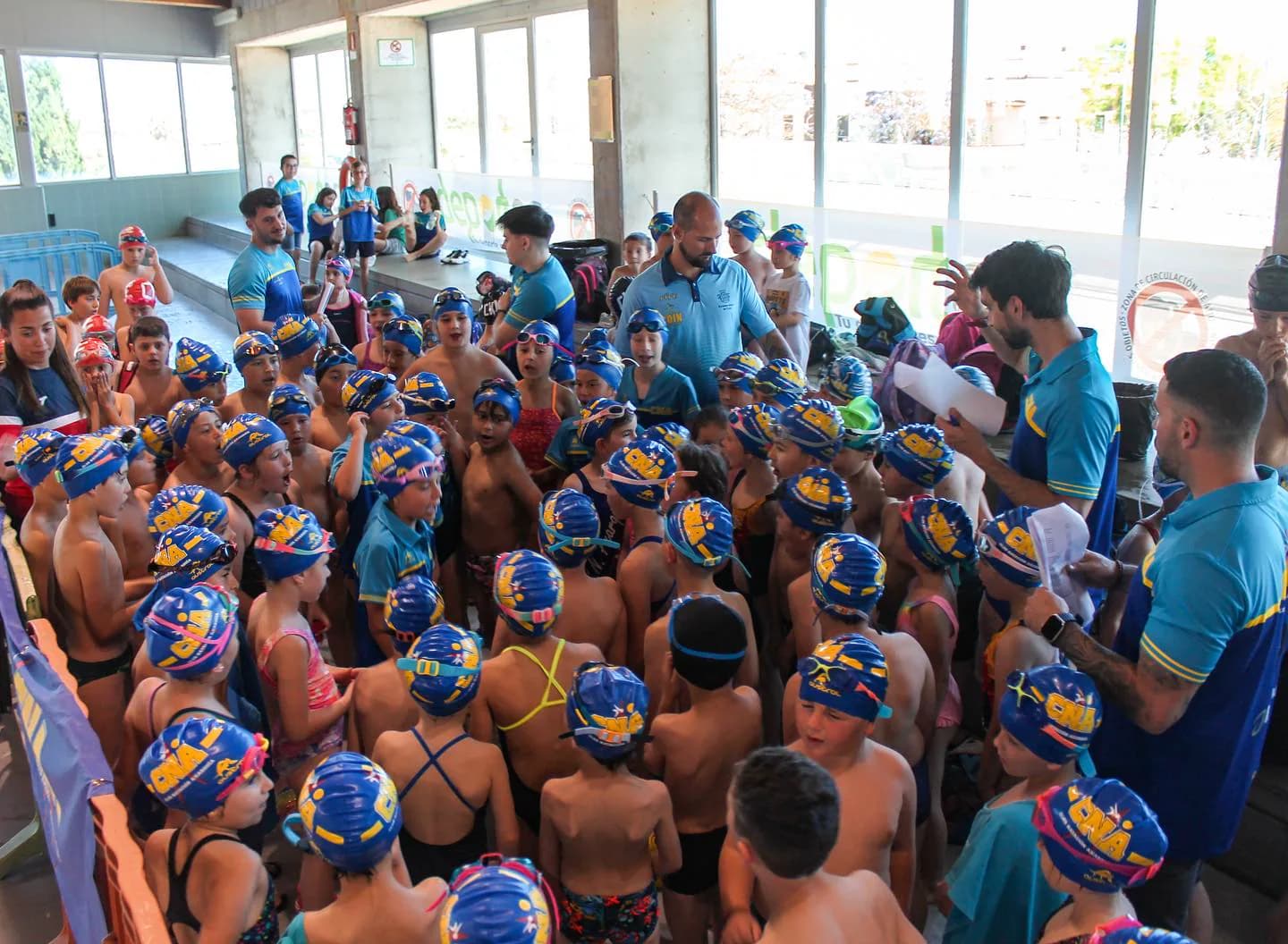 Coaches with many children in CNA caps, gathered beside the indoor pool at the XII Open Chupete